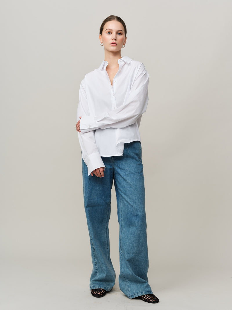 Person wearing a white shirt and blue jeans on a plain background